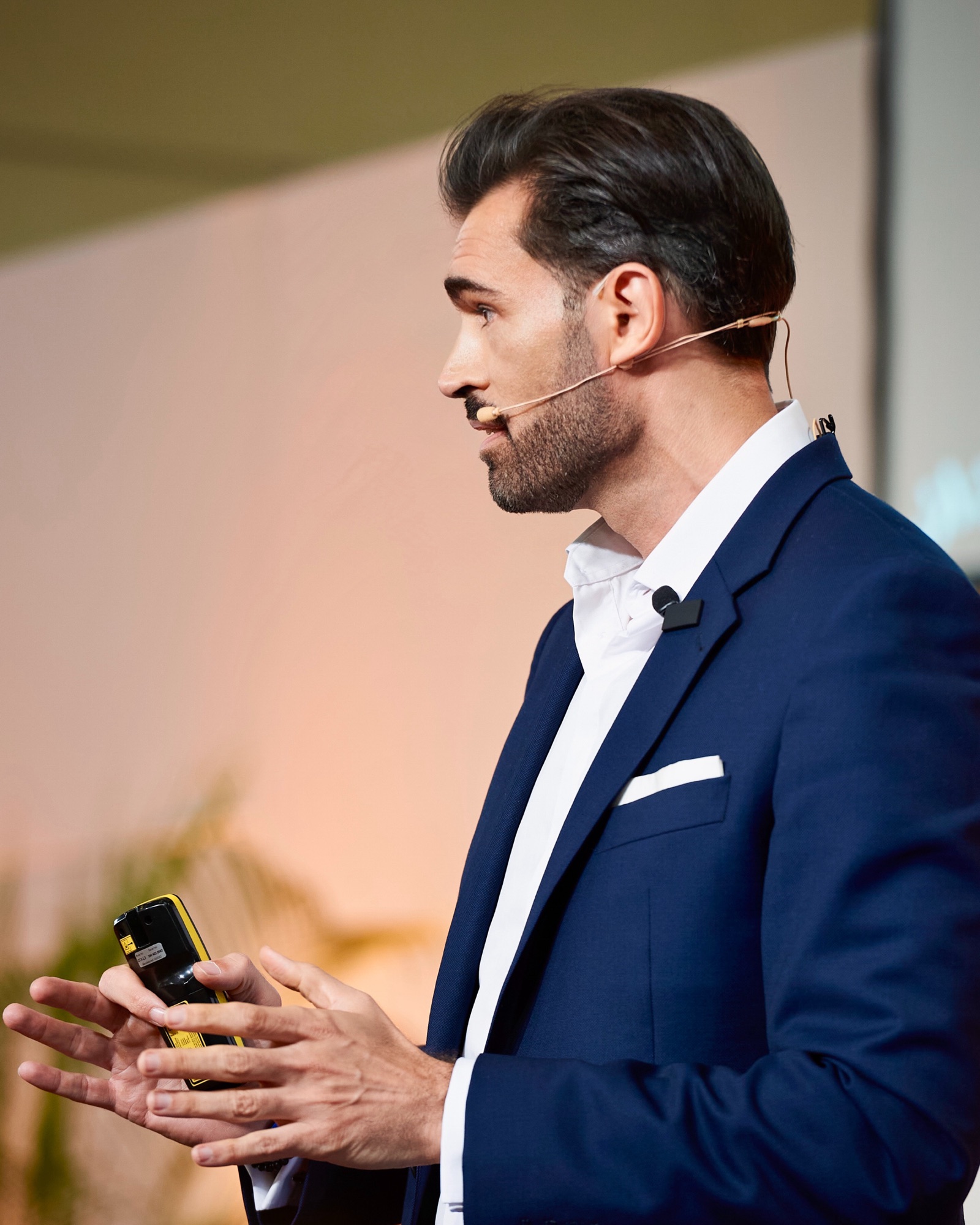 Alex Khan auf der Bühne, im Profil mit Headset, während eines Vortrags