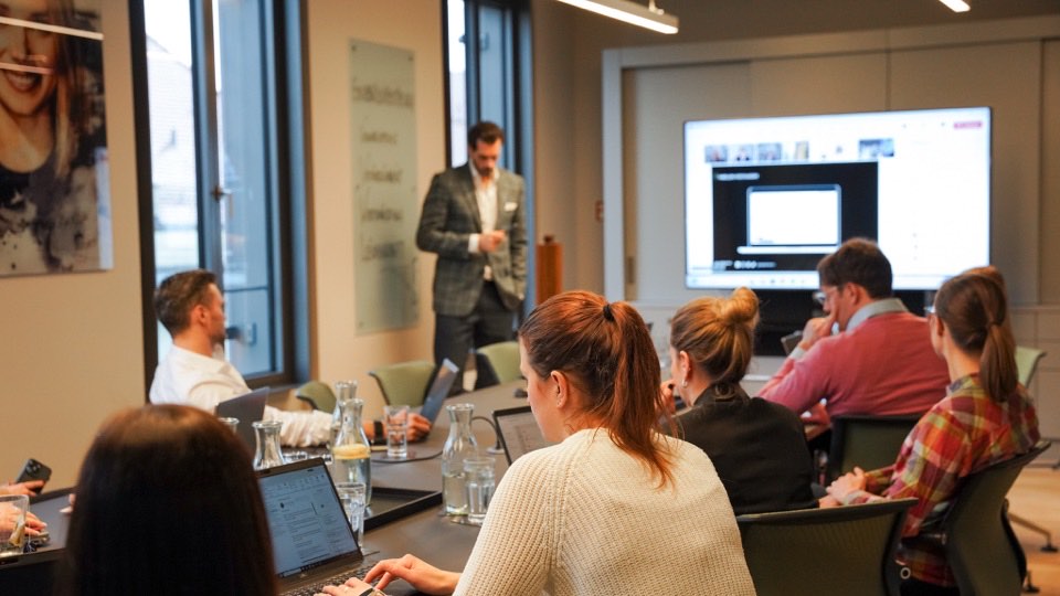 Teilnehmende eines KI-Workshops verfolgen eine Live-Demo von Alex Khan am großen Bildschirm