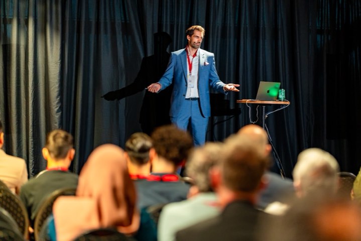 Alex Khan mit großer Geste auf heller Bühne